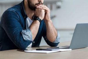 man thinking behind a laptop computer