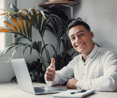Millenial man thumbs up sitting behind a laptop computer
