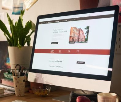 A desktop monitor on a wood desk showing a simple homepage, with a small plant beside it.